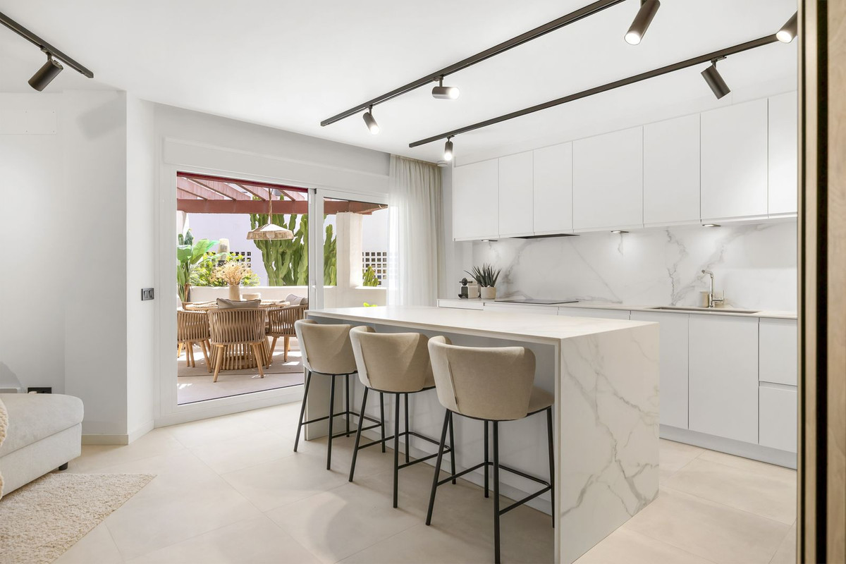 Fitted white kitchen with stone island opening onto the covered terrace